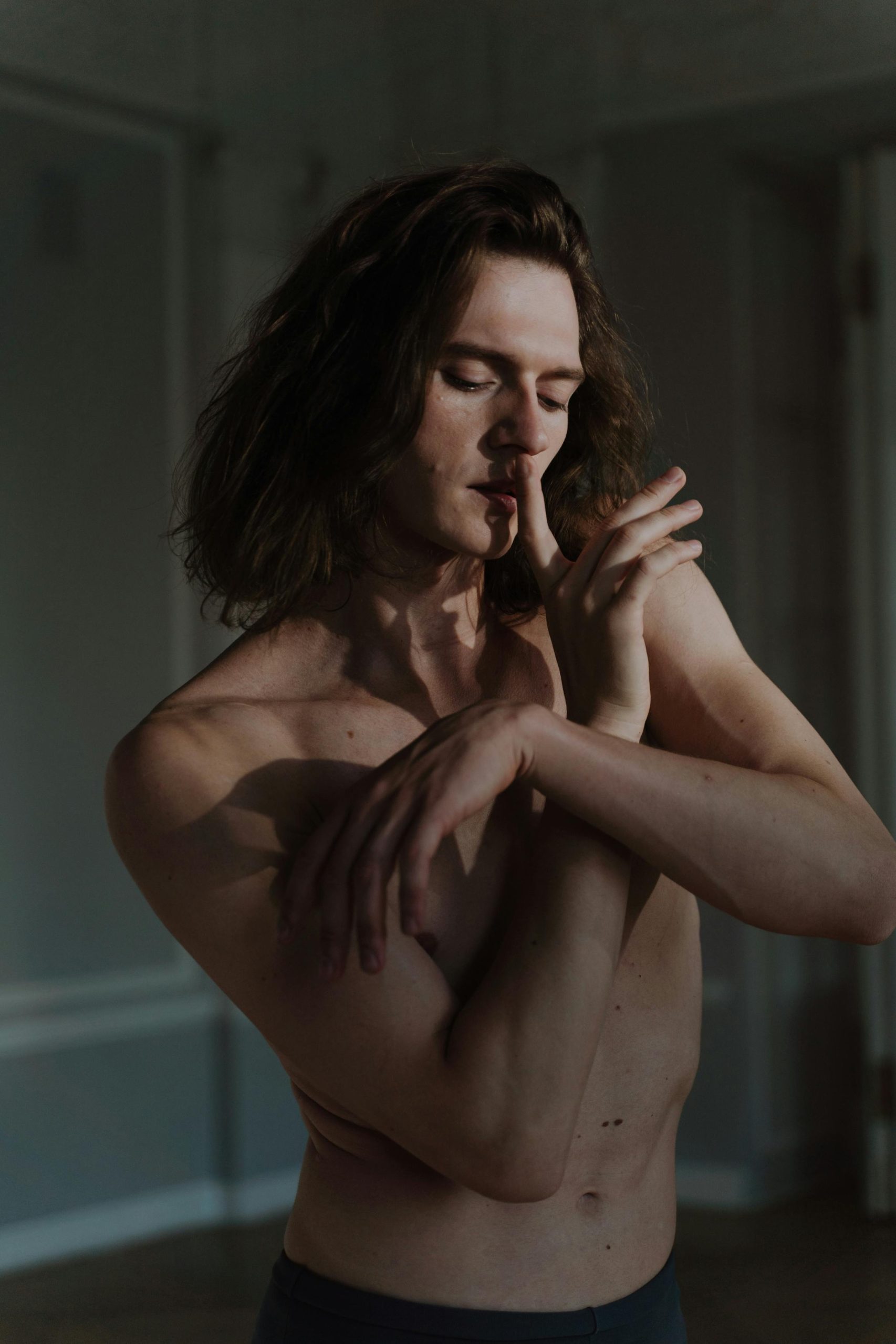 Artistic moody portrait of a shirtless male dancer indoors, emphasizing expressive hand gesture.